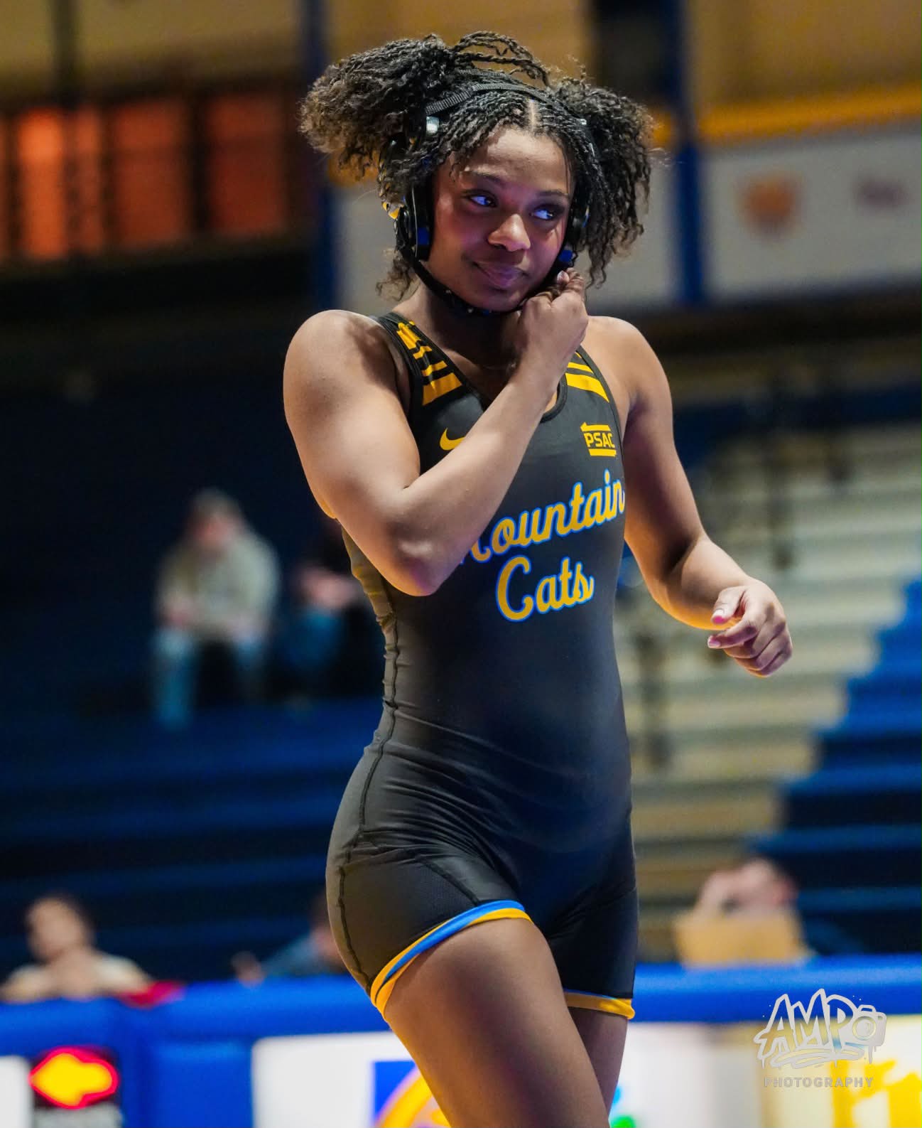 Tamara Humphries adjusting her headgear strap in a black and gold Mountain Cats singlet, looking off to the side.