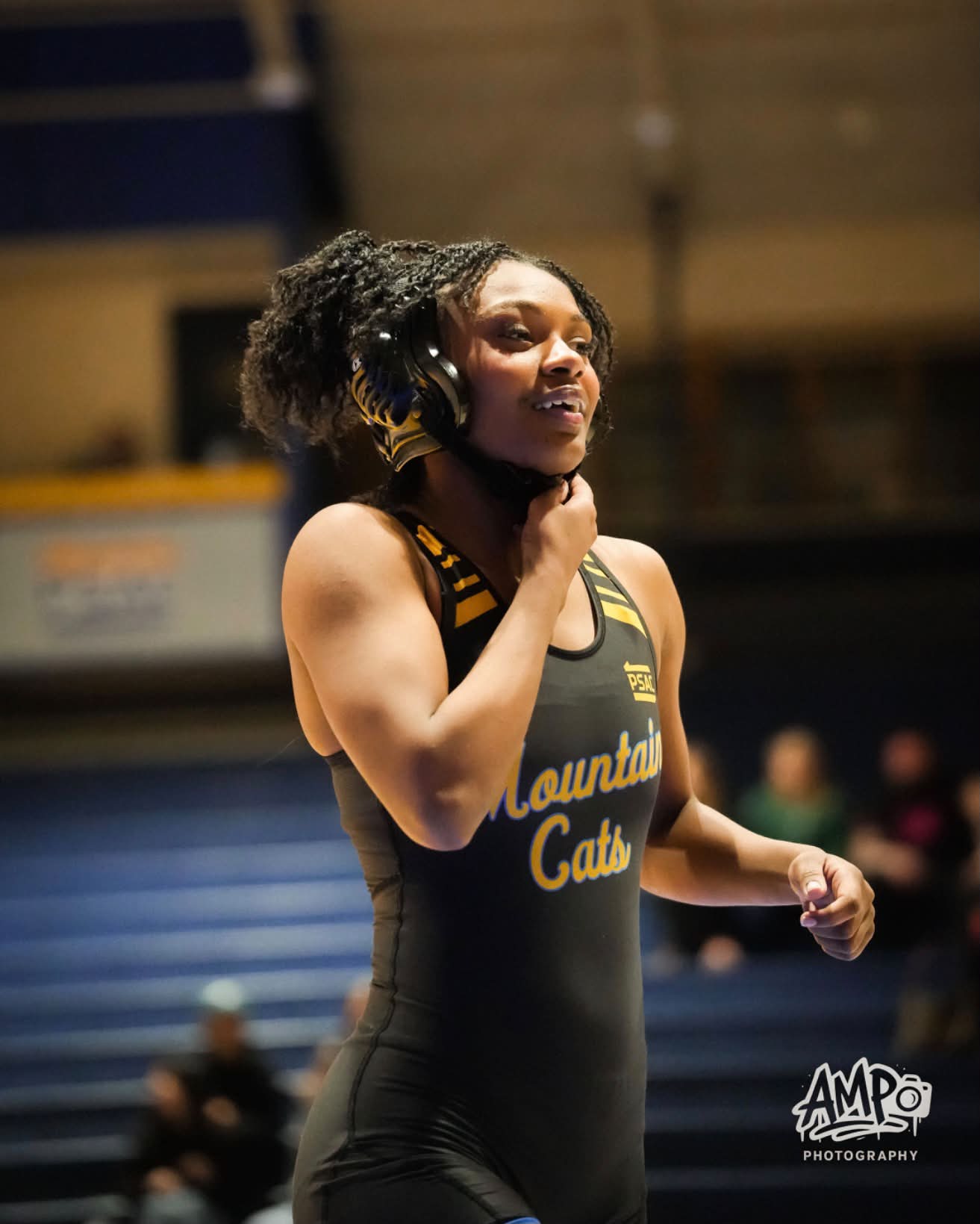 Tamara Humphries walking off the mat in her Mountain Cats singlet, headgear in hand, laughing.